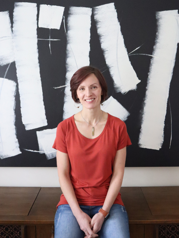 A picture of the artist Jennifer Rios from 1010artistry in front of one of her abstract paintings which is a large black background with white marks in different sizes
