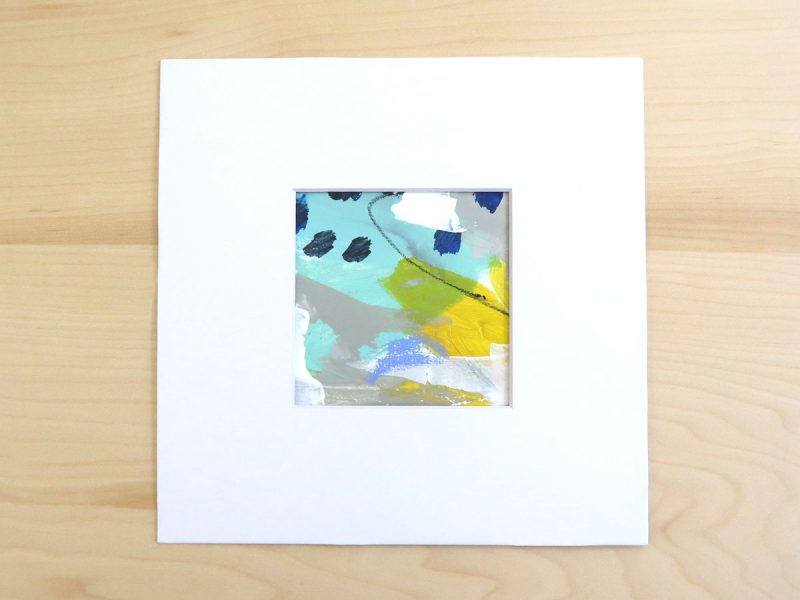 Small, square abstract painting in turquoise, yellow, gray and white shown matted on a wood background