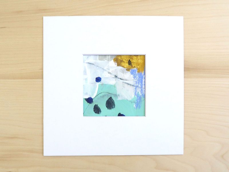 Small, square abstract painting in turquoise, yellow, gray and white shown matted on a wood background