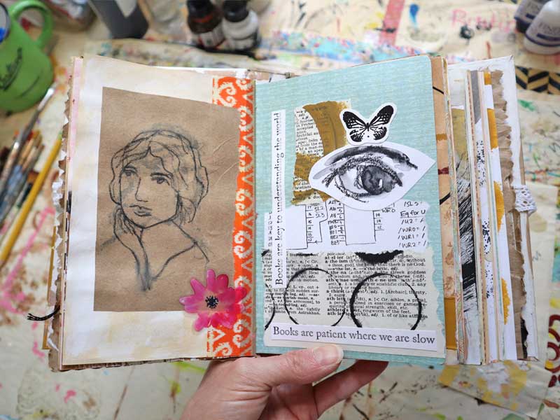 Collaged page in a hand bound art journal made with pieces of old homework, a dictionary page, a butterfly stamp, and a painting of an eye