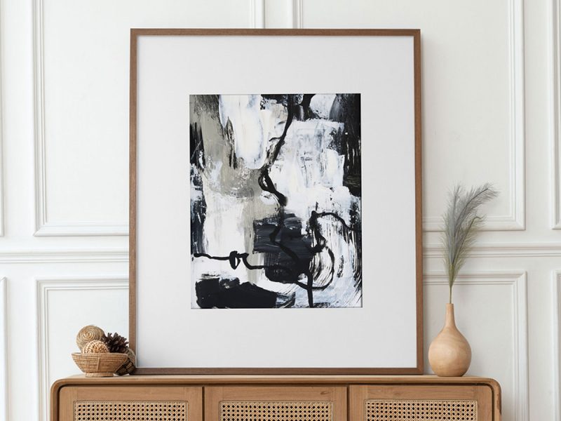Abstract painting of a background with scraped on paint in beige, black, grey and white with a black twisting line, shown framed and sitting on a wood console table.